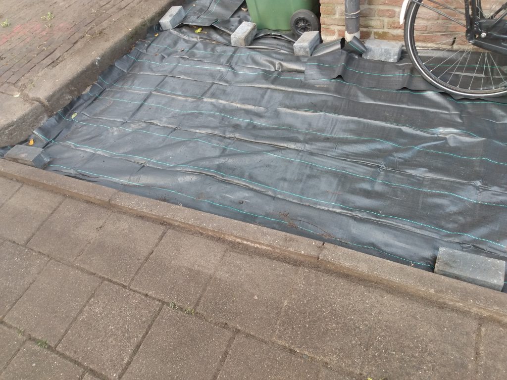 Grond afdekken met bouwfolie, afwerking met betonbanden. 
